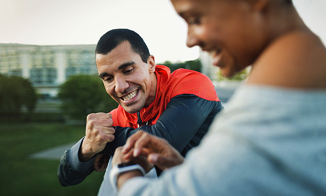 Man celebrating victory while woman checking time on smart watch