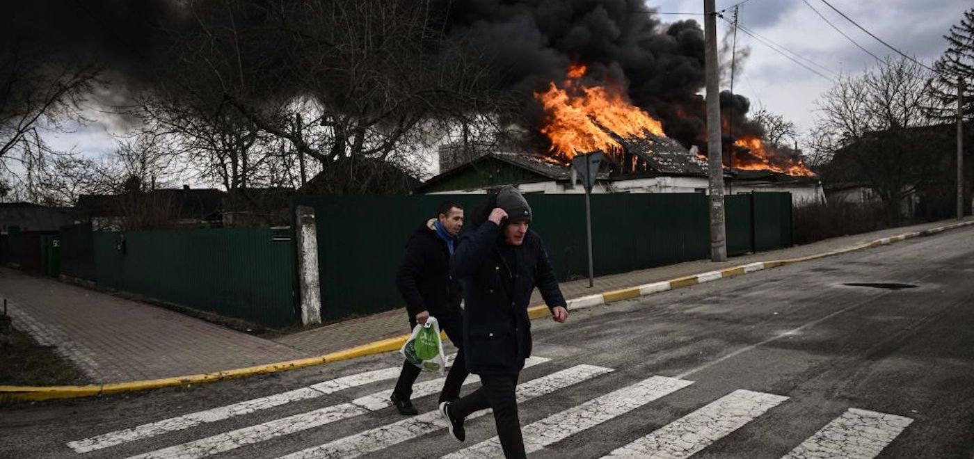 People run for cover in front of a burning house during shelling in the city of Irpin, outside Kyiv, on March 4, 2022